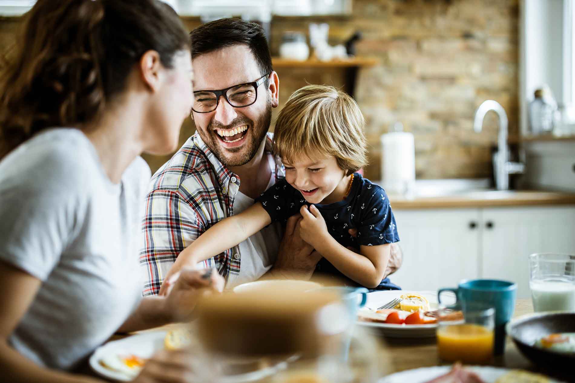 Husband holding son and laughing at dinner table with wife.